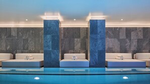 Un área de piscina interior moderna con tres zonas de estar, cada una con cojines y toallas enrolladas.