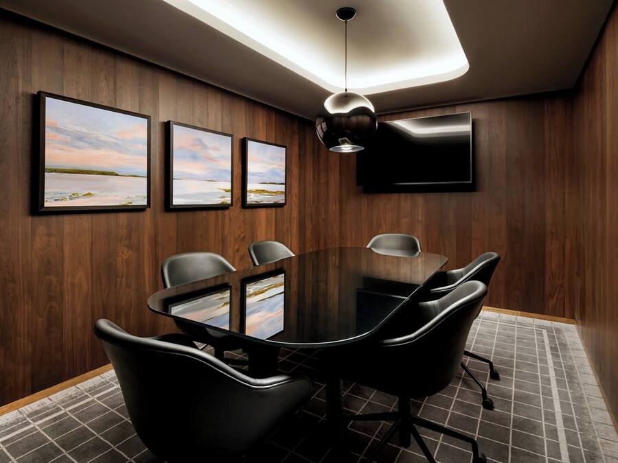 Een vergaderruimte met een glazen tafel, zwarte stoelen, ingelijste foto's, een flatscreen-tv en houten lambrisering.