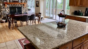 Une cuisine spacieuse dotée de plans de travail en granit, d’une cheminée en pierre et d’un coin repas avec un grand îlot central.
