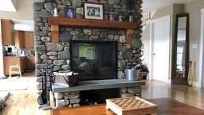 Une cheminée en pierre avec une étagère au-dessus, une table basse en bois et un jeu d’échecs.