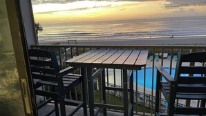 Un balcón con una mesa y sillas de madera, con vista a una piscina y una playa.