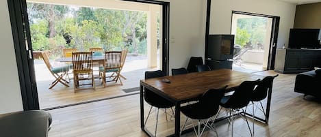 A modern living room with a wooden dining table, black chairs, and a TV.