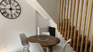 Ein Essbereich mit einem runden Holztisch, weißen Stühlen und einer schwarzen Wanduhr.