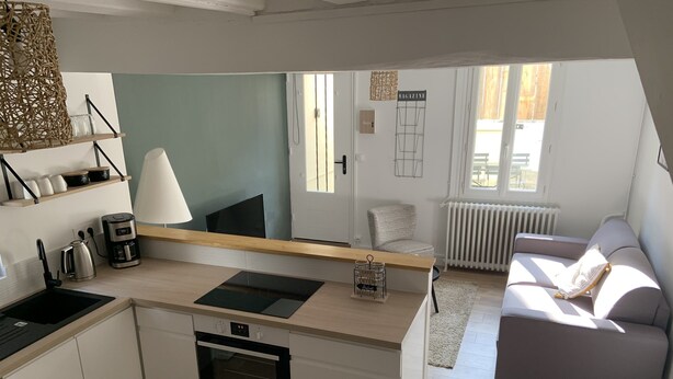 Eine kompakte Küche mit Einbauofen, Kaffeemaschine und Wasserkocher. Es gibt eine kleine Essecke mit Tisch und Stühlen. Der Raum verfügt über ein Sofa und eine Heizung.