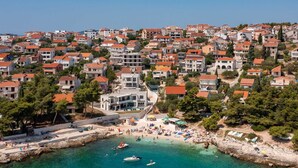A coastal town with a beach area, clear turquoise waters, and numerous buildings with red-tiled roofs.