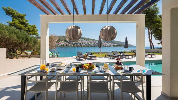 A dining area with a table set for breakfast, overlooking a pool and a scenic view of a coastal town.