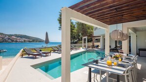 A poolside area with lounge chairs, a dining table set for breakfast, and a view of the sea.