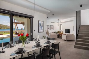 Een moderne eethoek met uitzicht op zee, een gezellige woonkamer met een televisie, en een trap.