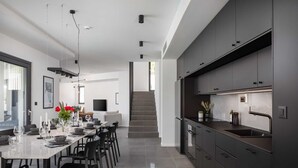 A modern kitchen with dark cabinetry, a dining area with a long table and chairs, and a staircase leading to an upper level.