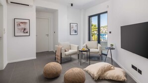 A modern living room with a large TV, two sofas, a small table, and a balcony with a view.