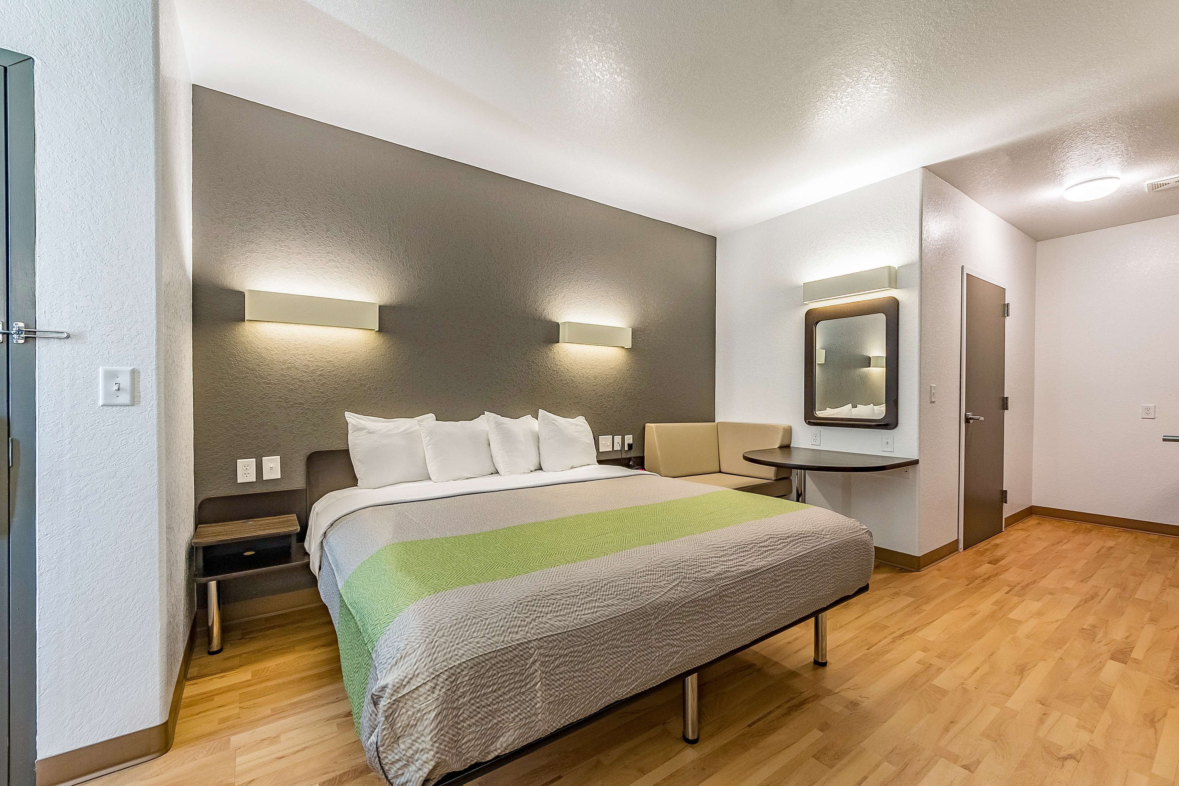 A modern hotel room with a large bed, bedside tables, a small desk, and a mirror.