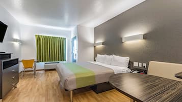A modern hotel room with a bed, a desk, a chair, and a television.