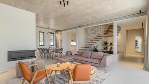 Een moderne woonkamer met een bank, fauteuils, een salontafel en een open haard.