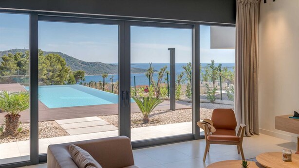 Een moderne kamer met een grote schuifglazen deur die uitkomt bij een buitenzwembad en uitzicht op zee.