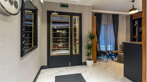 Eine Hotelhalle mit einer schwarzen und goldenen Tür, einer großen Wanduhr, einem Blumentopf und einer Sitzecke mit Tisch und Stühlen.