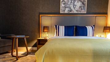 Ein Hotelzimmer mit einem großen Bett, einem Nachttisch, einer Lampe, einem gerahmten Bild an der Wand und einem kleinen Beistelltisch.