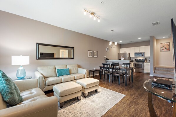 A modern living room with a sofa, ottomans, a coffee table, and a dining area with chairs and a table. - Resort Amenities Included! (Kissimmee)