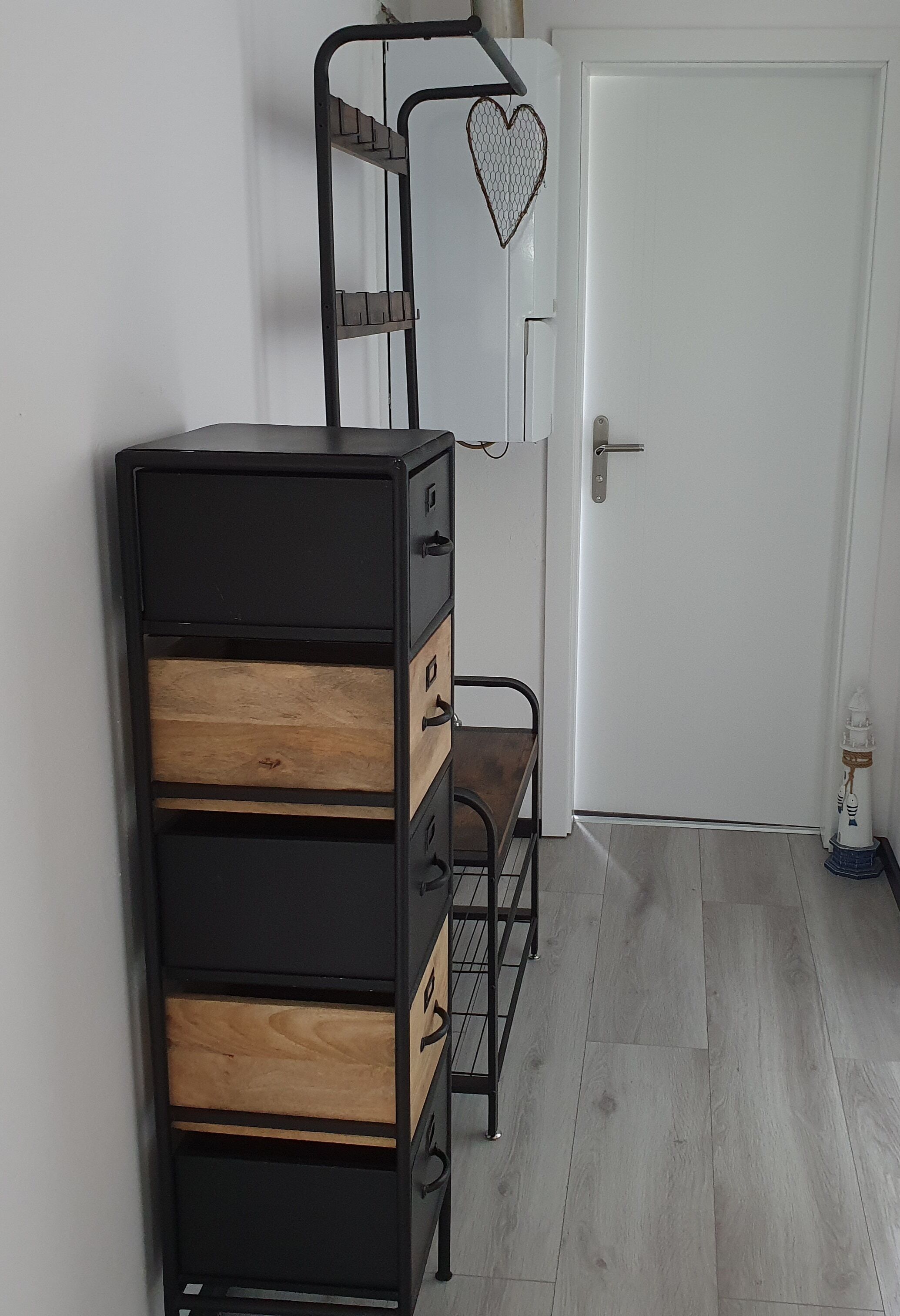 A room with a black metal dresser with wooden drawers, a white door, and a small white object on the floor.