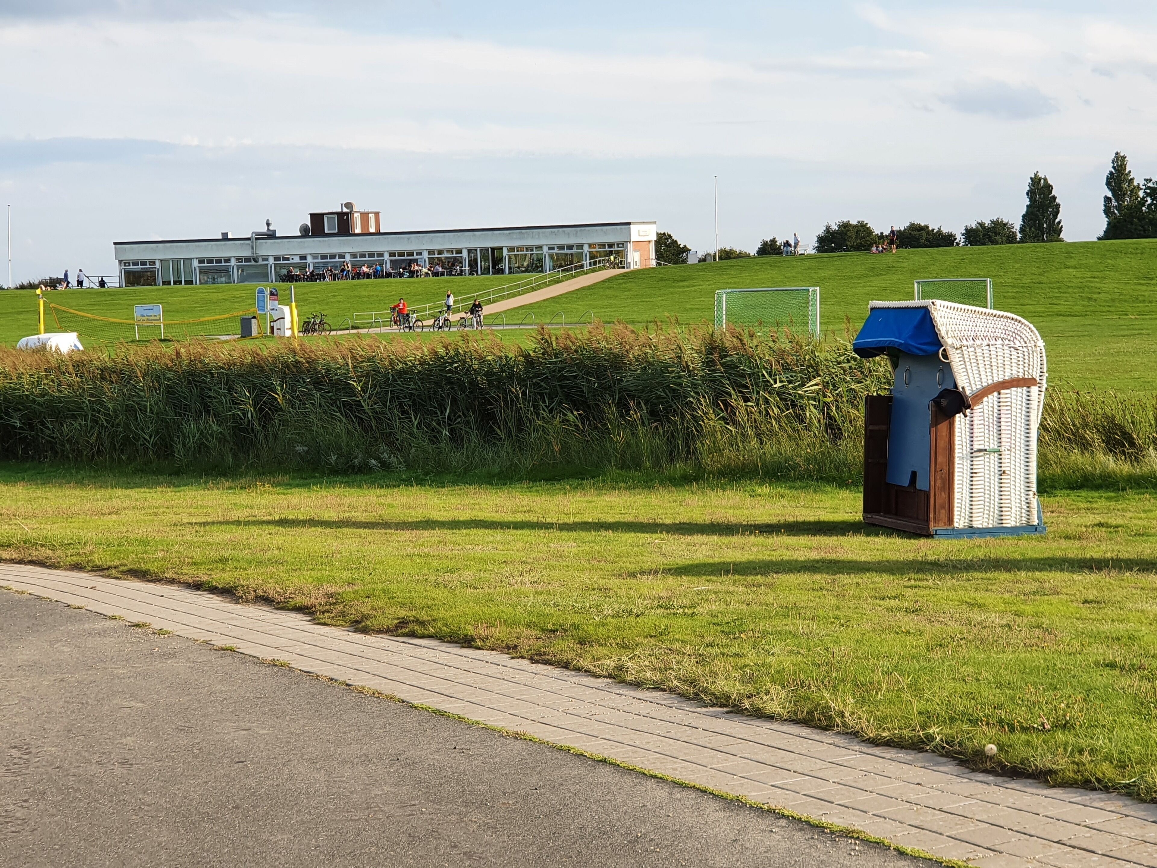 A grassy area with a small structure, a paved path, and a building in the background.