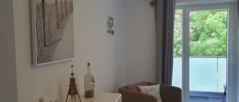 Ett rum med ett stort fönster, en soffa, en byrå och en vägg med ett inramat konstverk och en skylt.