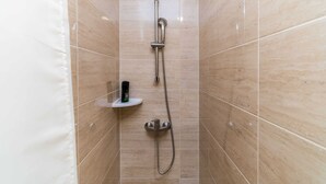 Une petite cabine de douche carrelée, dotée d’un pommeau de douche à main et d’un robinet fixé au mur.
