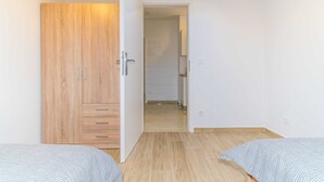 Une chambre avec une armoire en bois, deux lits et un couloir menant à une autre pièce.