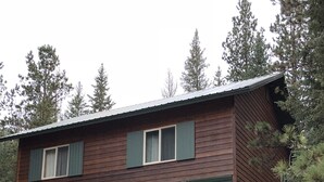 A two-story wooden cabin with a porch, wooden chairs, and a gravel driveway. - Rapid Creek Get Away (Hill City)
