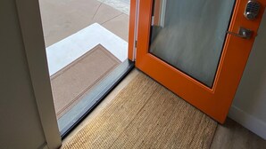 Hoteleingang mit Glastür, Blick auf den Strand und ein Parkplatz.