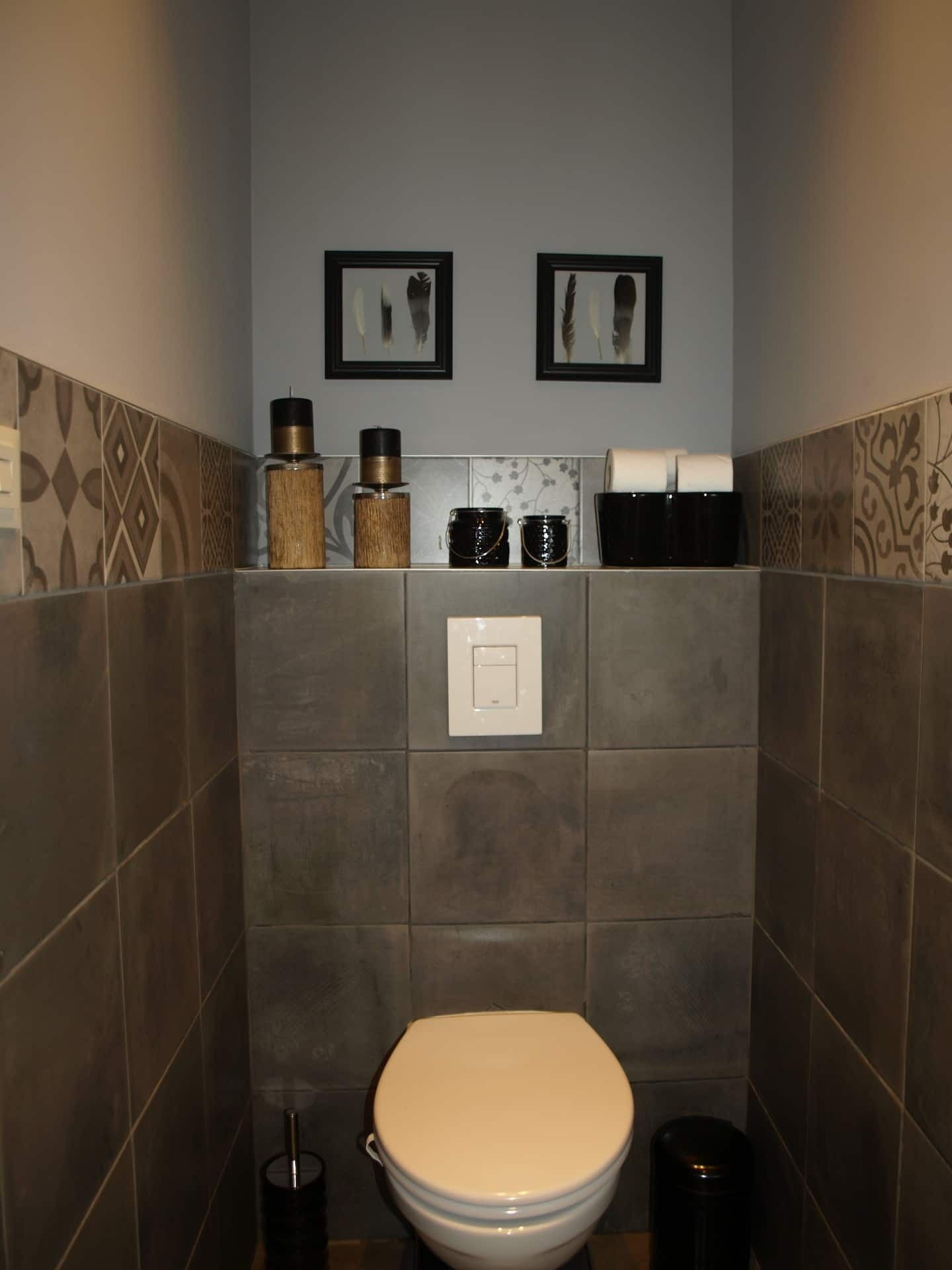 A bathroom with a toilet, a shelf with toiletries, and two framed pictures on the wall.