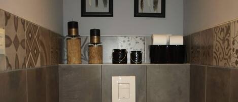 A bathroom with a toilet, a shelf with toiletries, and two framed pictures on the wall.