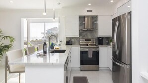 A modern kitchen with a central island, stainless steel appliances, and a view of the city. - Beautiful Remodeled Oceanfront Condo ~ Best Location and Spectacular Views! (Saint Augustine)