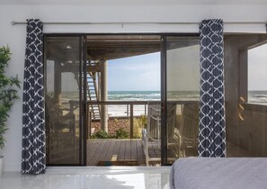 A room with a large sliding glass door leading to a balcony with a view of the ocean.