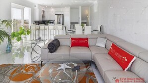 A modern living room with a sofa, a coffee table, and a kitchen in the background. - Beautiful Remodeled Oceanfront Condo ~ Best Location and Spectacular Views! (Saint Augustine)