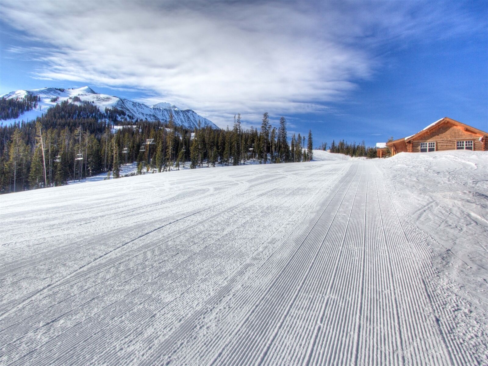 Une piste de ski enneigée, avec un chalet et une montagne en arrière-plan.
