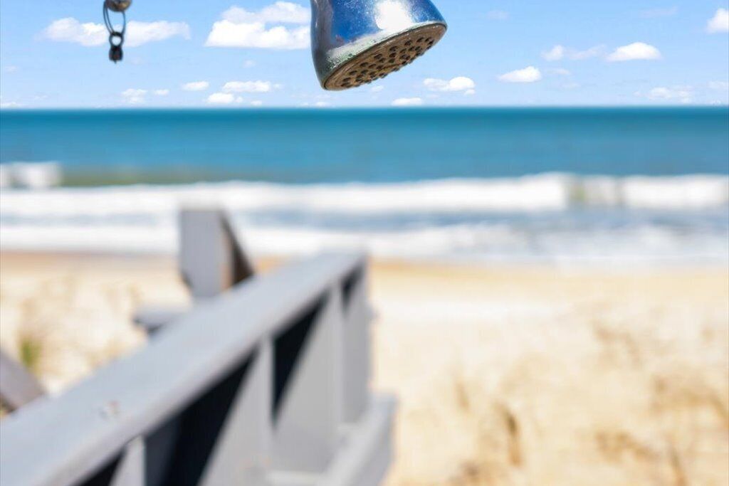 A beach scene with a metal object hanging above the sand, a wooden fence in the foreground, and the ocean in the background.
