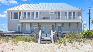Ein zweistöckiges Strandhaus mit Balkon, einer Veranda und einer Treppe, die zum Eingang führt.