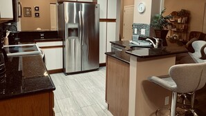 A modern kitchen with a stainless steel refrigerator, a built-in oven, and a sink with a bar stool.