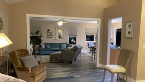 A spacious living room with a sofa, armchairs, and a dining area in the background.