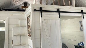 Dormitorio estilo loft con techo de madera, cama en altura, puerta corrediza tipo granero y una pequeña escalera.