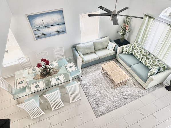 Uma sala de estar moderna com uma mesa de jantar de vidro, cadeiras brancas, um sofá e um ventilador de teto.