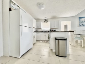 Uma cozinha moderna com armários brancos, uma lixeira de aço inoxidável e uma área de refeições com cadeiras brancas.