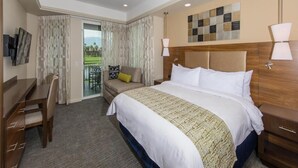 Une chambre d’hôtel avec un grand lit, un bureau, une chaise, une table de chevet et une vue sur un paysage verdoyant, visible à travers une porte vitrée.