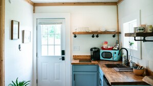 Eine Küche mit einer weißen Tür, einem Fenster und einer Arbeitsplatte mit Kaffeemaschine, Mikrowelle und Regalen darüber.