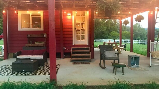 Eine rote Holzkonstruktion mit überdachter Terrasse, möbliert mit Sitzgelegenheiten und einer Treppe zu einer oberen Ebene.