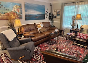 A living room with a brown leather sofa, a patterned rug, and a wall with a painting and a guitar.