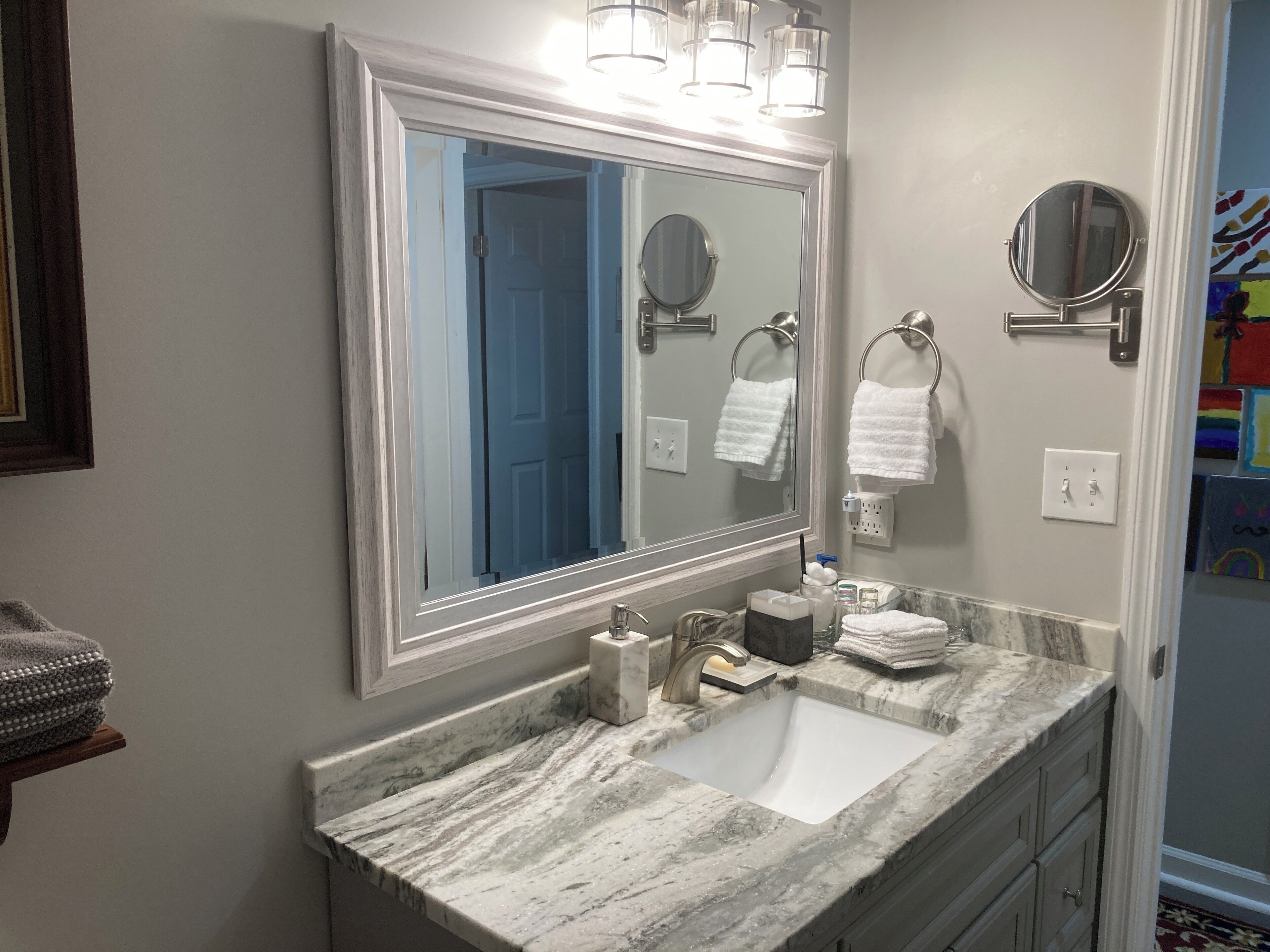 A bathroom with a large mirror, a sink, and two towel rings.