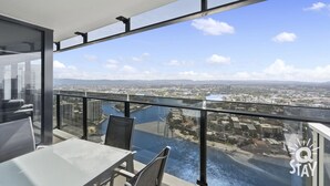 A balcony with a glass railing overlooking a cityscape and a body of water. - 1 Bedroom + Study SPA on High Floor — Q Stay (Surfers Paradise)
