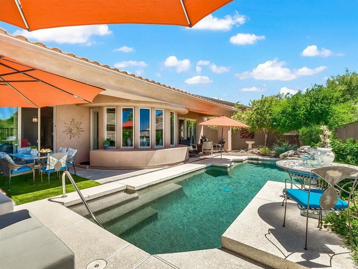 A swimming pool with a sunburst wall design, outdoor seating, and a covered patio area.