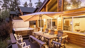 A wooden deck with a hot tub, wooden table, and chairs, and a large umbrella providing shade. - Big Bear Biltmore. Walk to the Park and Lake. Spa. (Big Bear Lake)