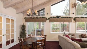 A dining area with a round table and chairs, a sofa, and a large window with a view of the outdoors. - Big Bear Biltmore. Walk to the Park and Lake. Spa. (Big Bear Lake)